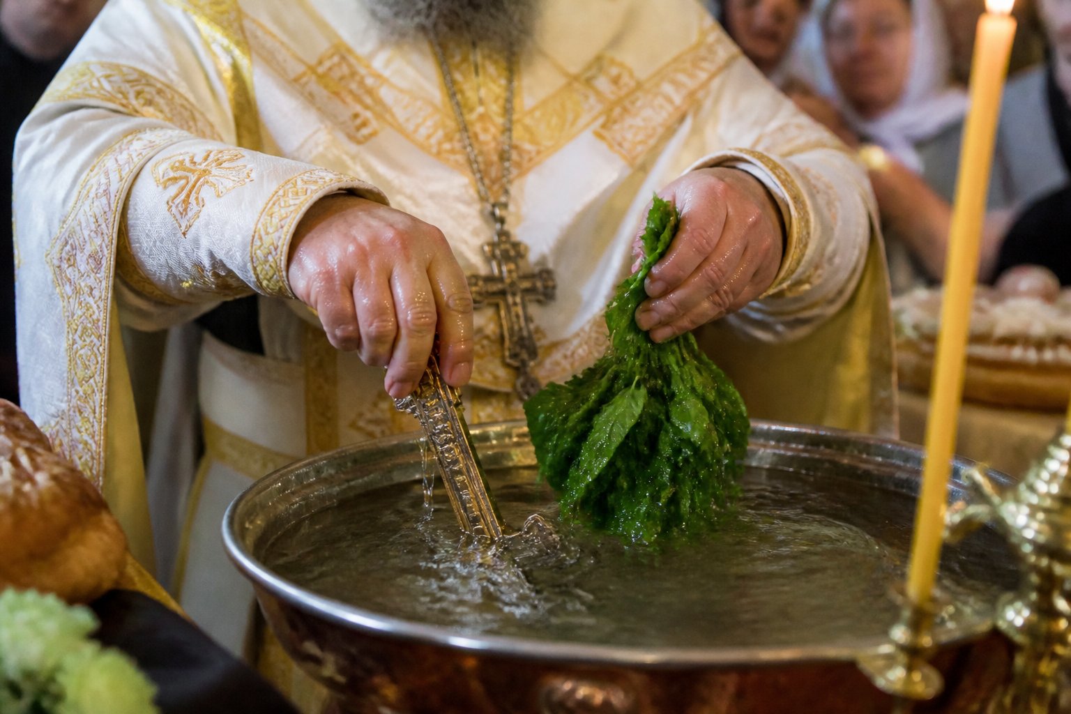 Preot binecuvântând apa (Agheasma) cu o cruce și busuioc, într-o ceremonie ortodoxă.